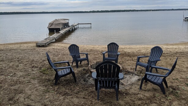 A lakeside setting with a wooden dock extending into the water, surrounded by chairs and a covered structure.
