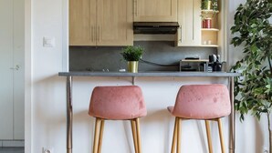 Eine moderne Küche mit Holzausziehtischen, einer schwarzen und goldenen Pendelleuchte sowie zwei pinkfarbenen Barhocker.