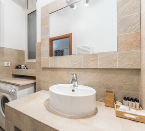 Un bagno con un lavandino rotondo, uno specchio sopra e una lavatrice a sinistra.