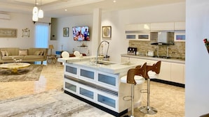 A modern kitchen with a central island, bar stools, and a dining area with a sofa and coffee table. -  Villa Yenne Dakar Diamniadio (Sendou)