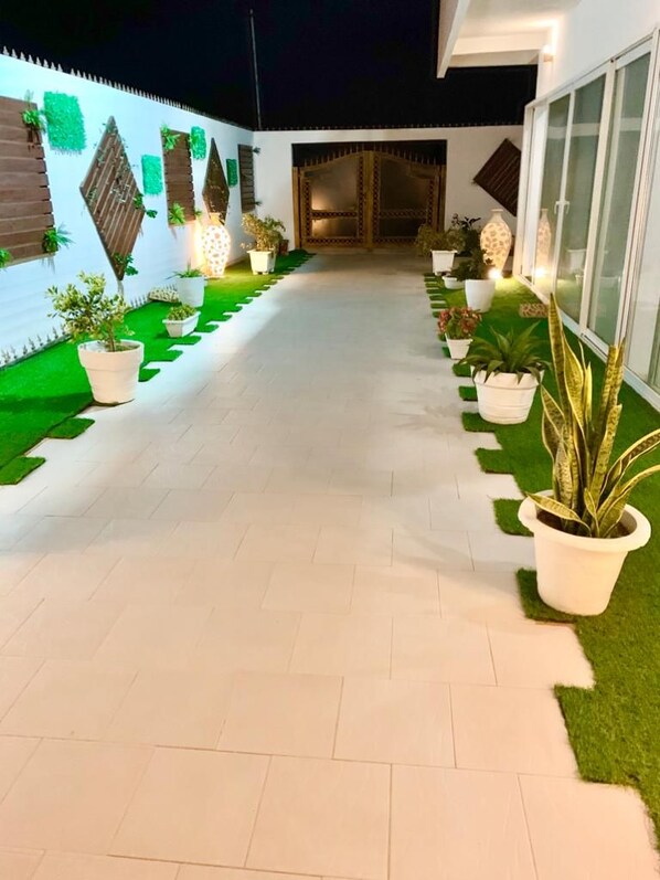 A well-lit pathway with potted plants and a green artificial turf area, leading to a building entrance. -  Villa Yenne Dakar Diamniadio (Sendou)