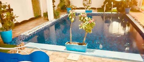 Une piscine intérieure avec un sol carrelé, des plantes en pot et un banc.