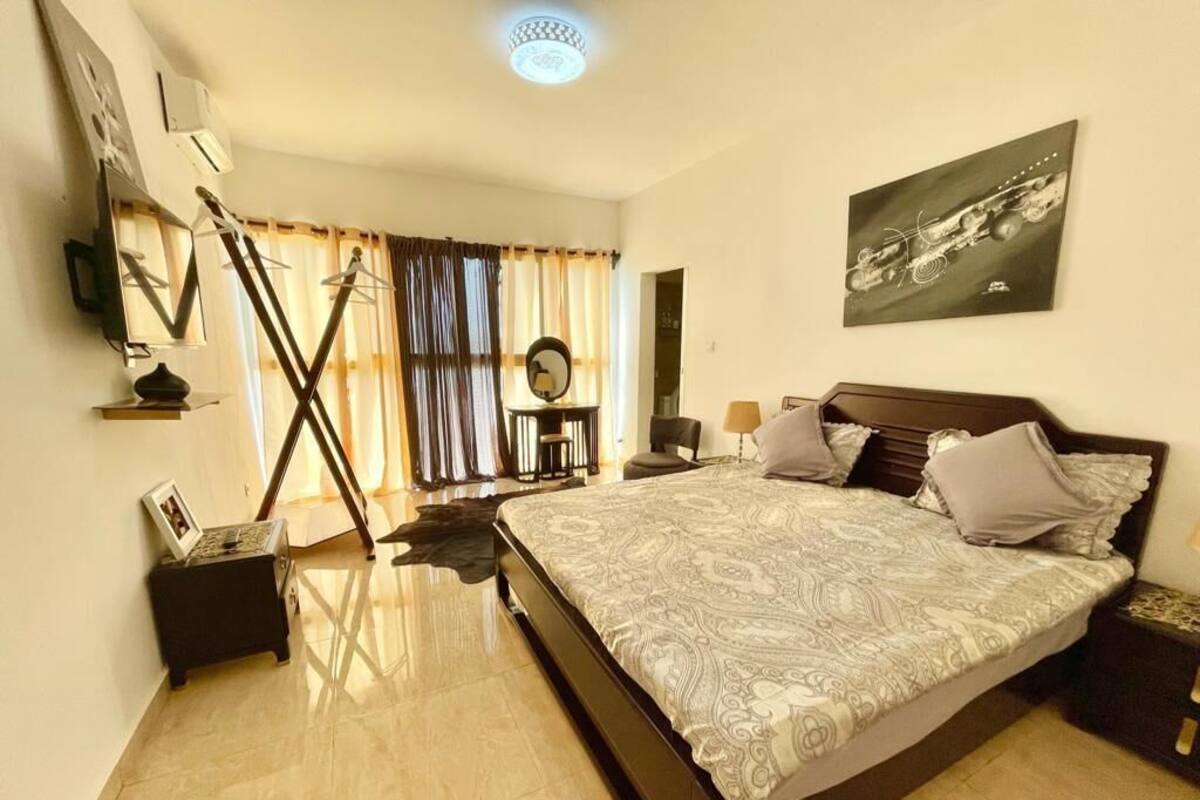 Un dormitorio con una cama grande, una mesita de noche, una silla, un espejo y una ventana con cortinas.