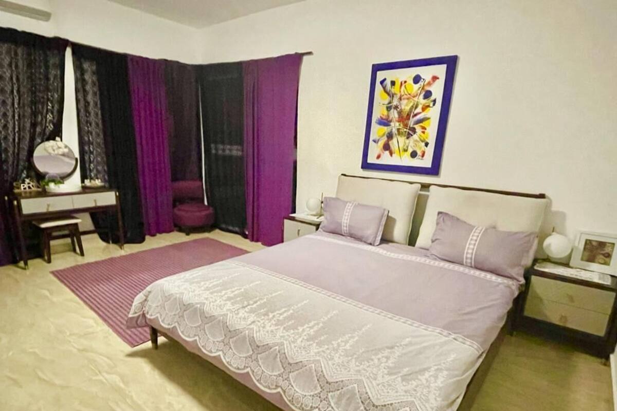 Un dormitorio con una cama grande, un escritorio con silla, un tocador y cortinas moradas.