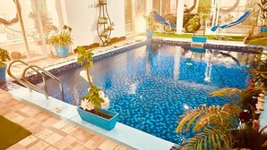An indoor swimming pool with a tiled edge, surrounded by potted plants and lounge chairs. -  Villa Yenne Dakar Diamniadio (Sendou)