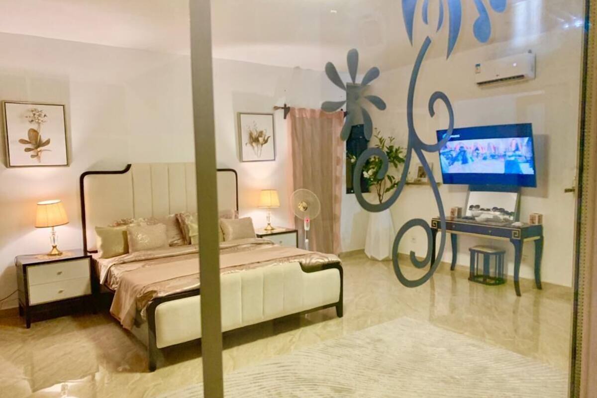 Un dormitorio con cama, mesitas de noche, televisión y decoración mural.