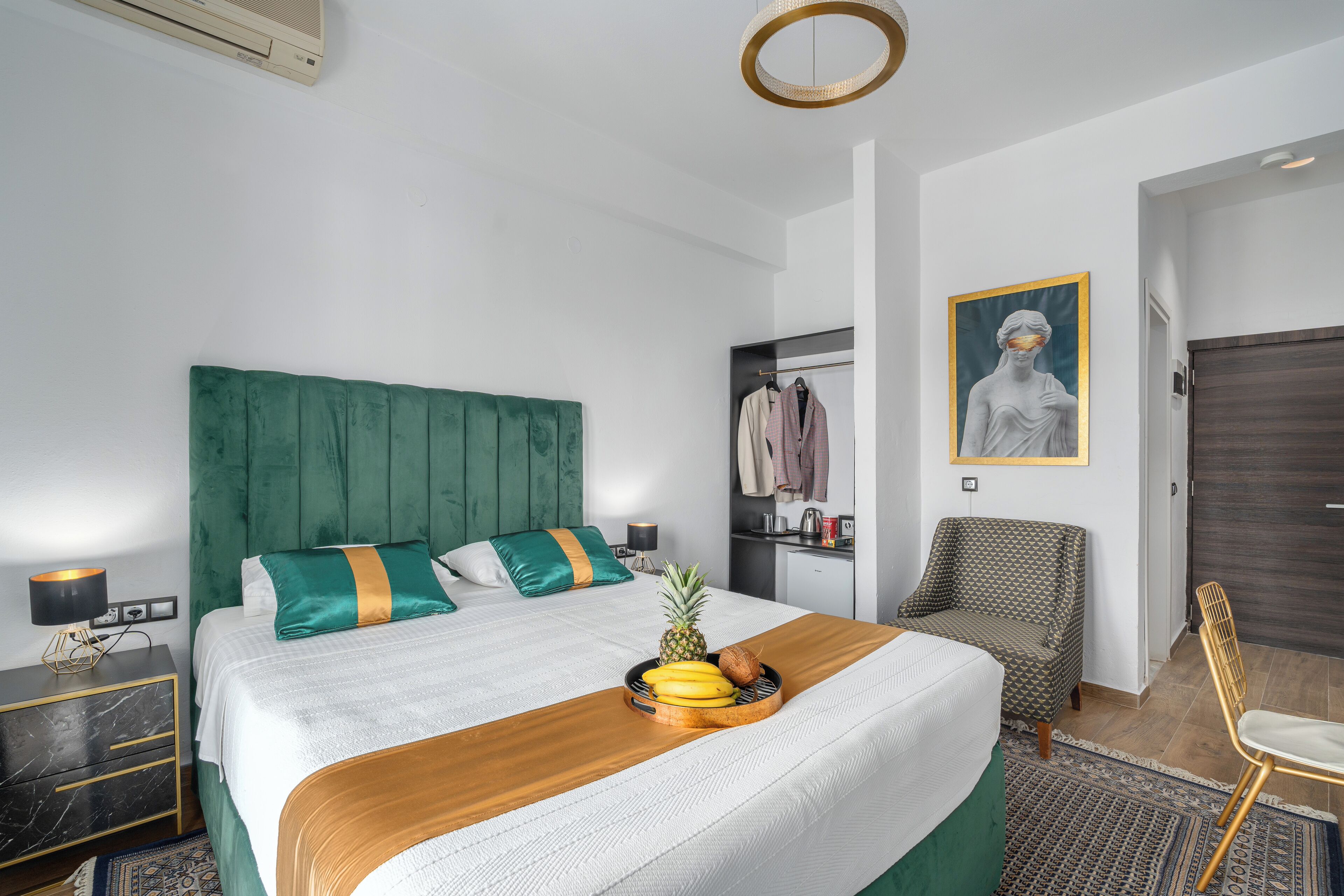 Una habitación de hotel ordenada con una cama grande, una mesita de noche, una silla y un escritorio pequeño con una lámpara.