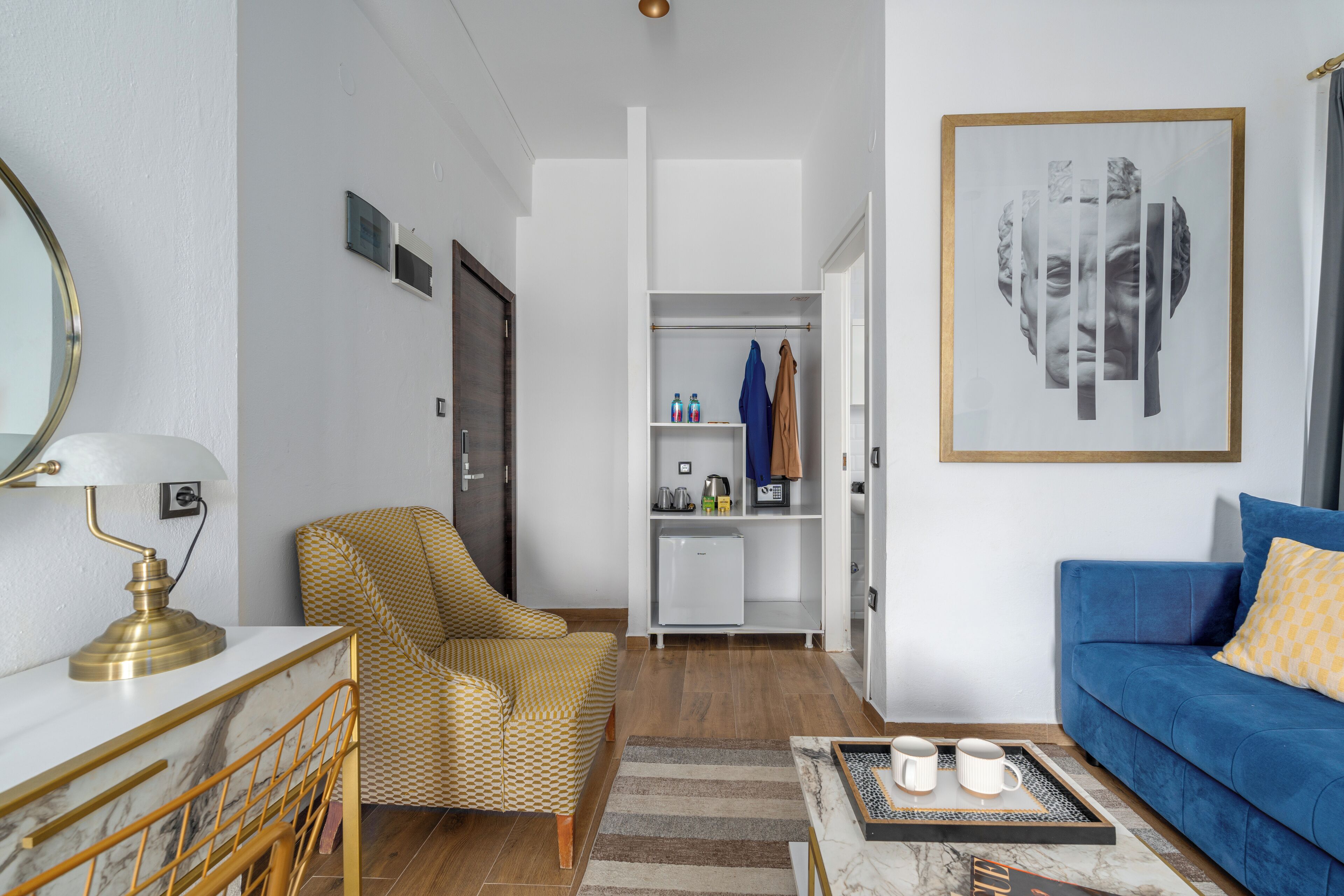 A modern living room with a sofa, armchair, coffee table, and a small refrigerator.
