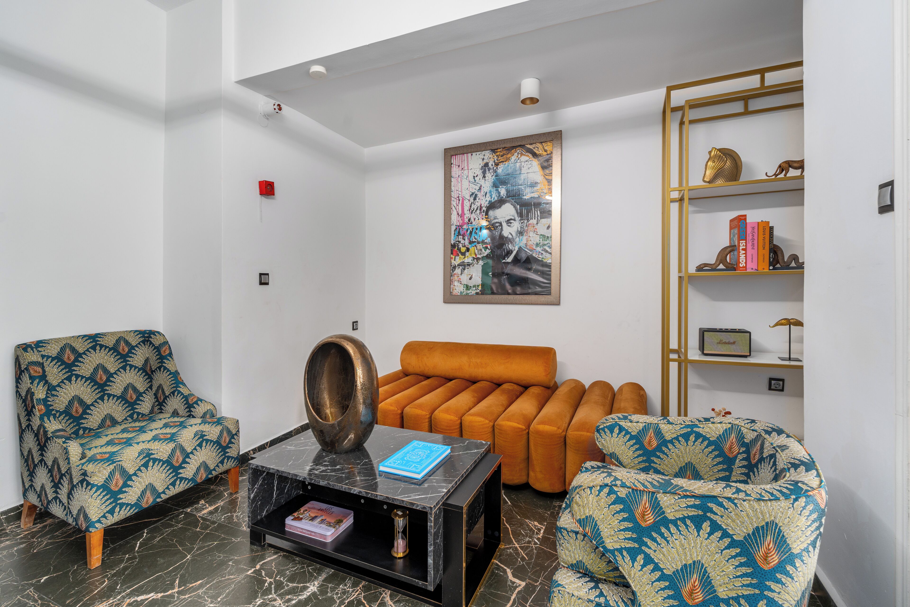 A living room with patterned armchairs, a sofa, a coffee table, and a bookshelf.