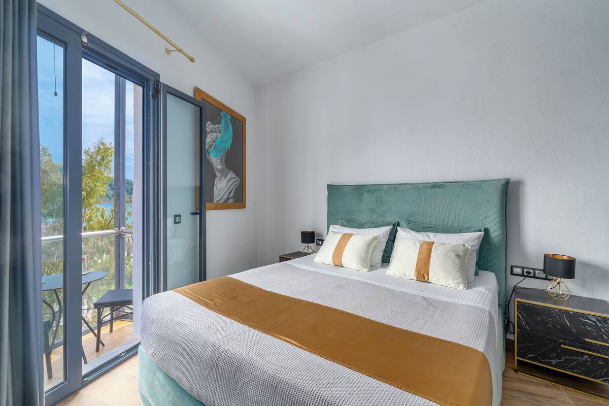 A modern bedroom with a large bed, a teal headboard, and a balcony with a table and chairs.