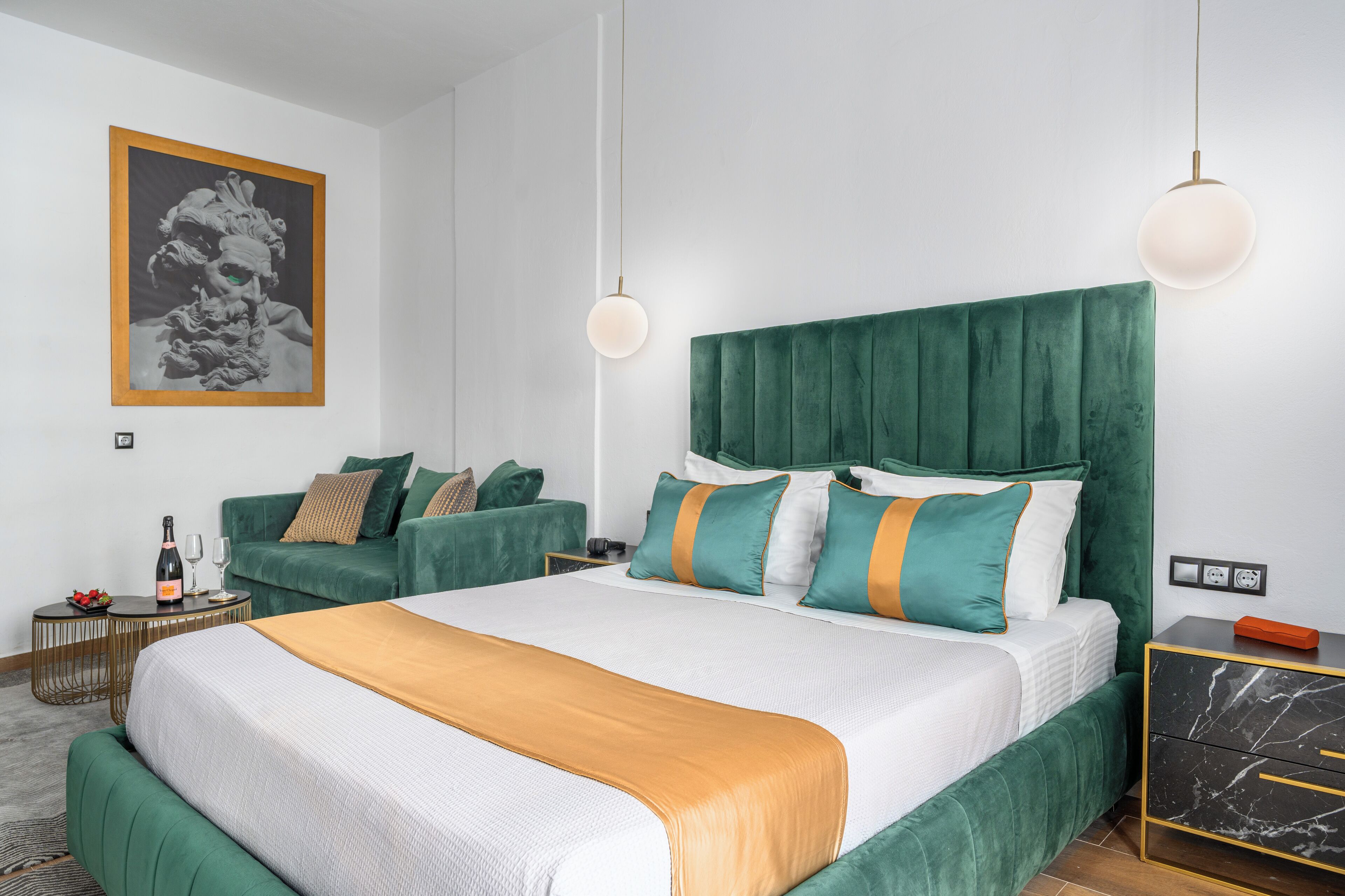 Ett modernt hotellrum med en stor säng, en grön klädd sänggavel och en grön soffgrupp.