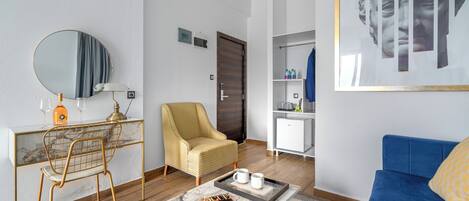 Una sala de estar moderna con un sofá, una mesita de centro con una revista, una silla, un escritorio con un espejo y un armario.