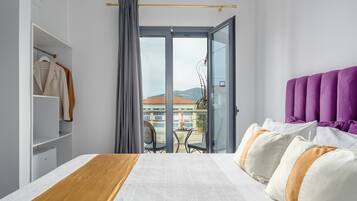 Habitación de hotel con cama, armario, balcón con mesa y sillas, y vistas a edificios y colinas.