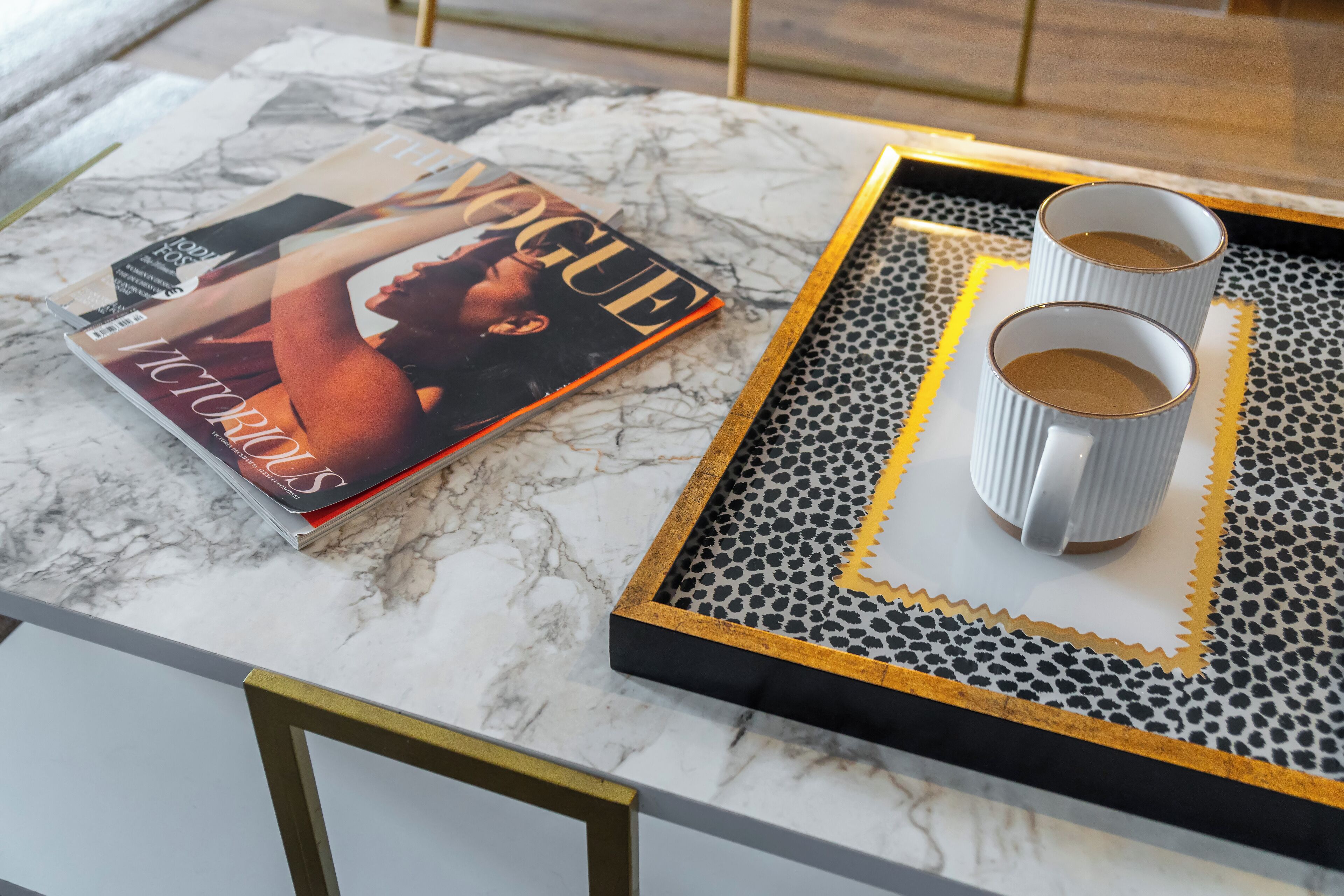 Una revista sobre una mesa de mármol con una bandeja de dos tazas de café.