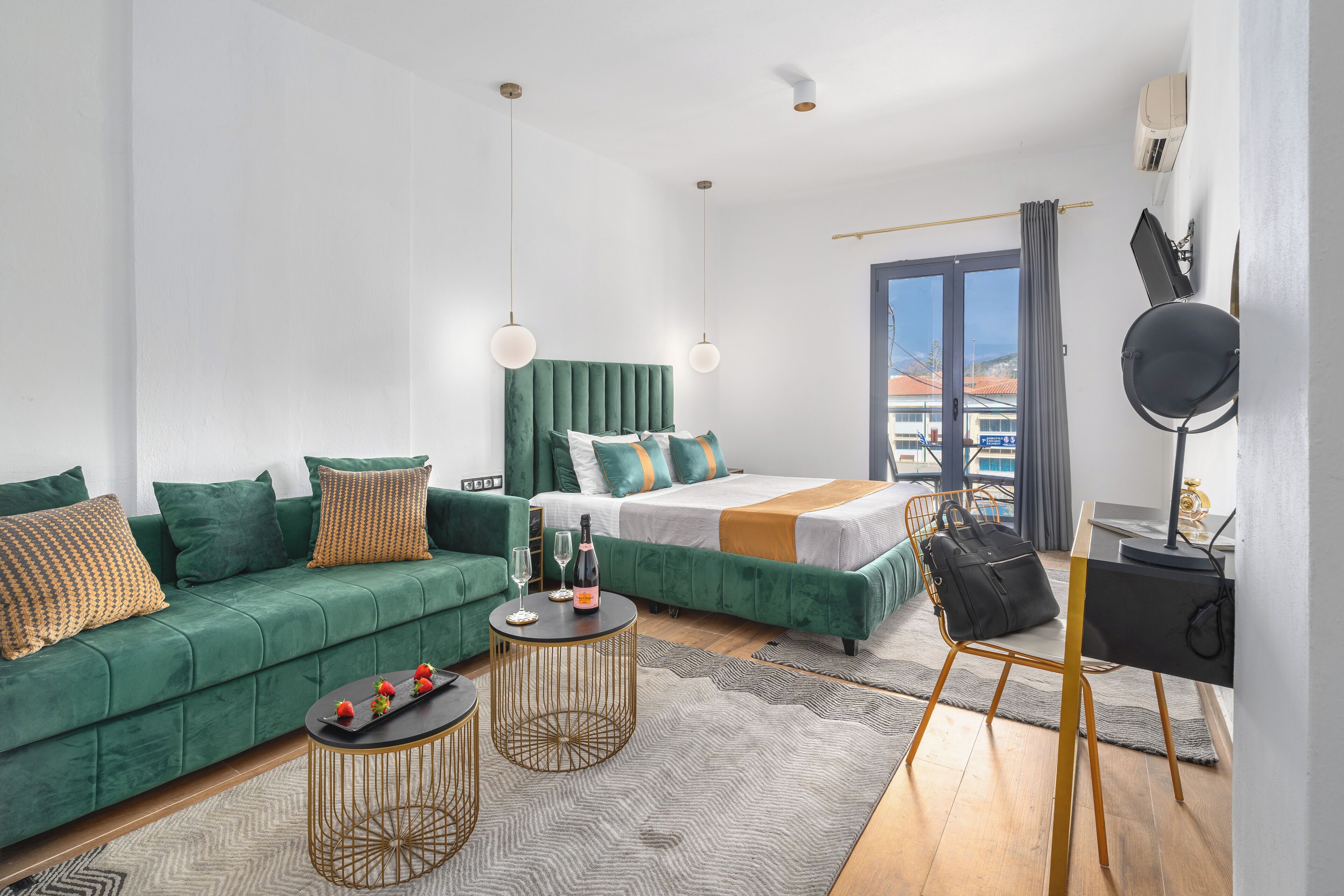 A modern hotel room with a green sofa, a bed with a green headboard, a round gold table, and a desk with a chair.