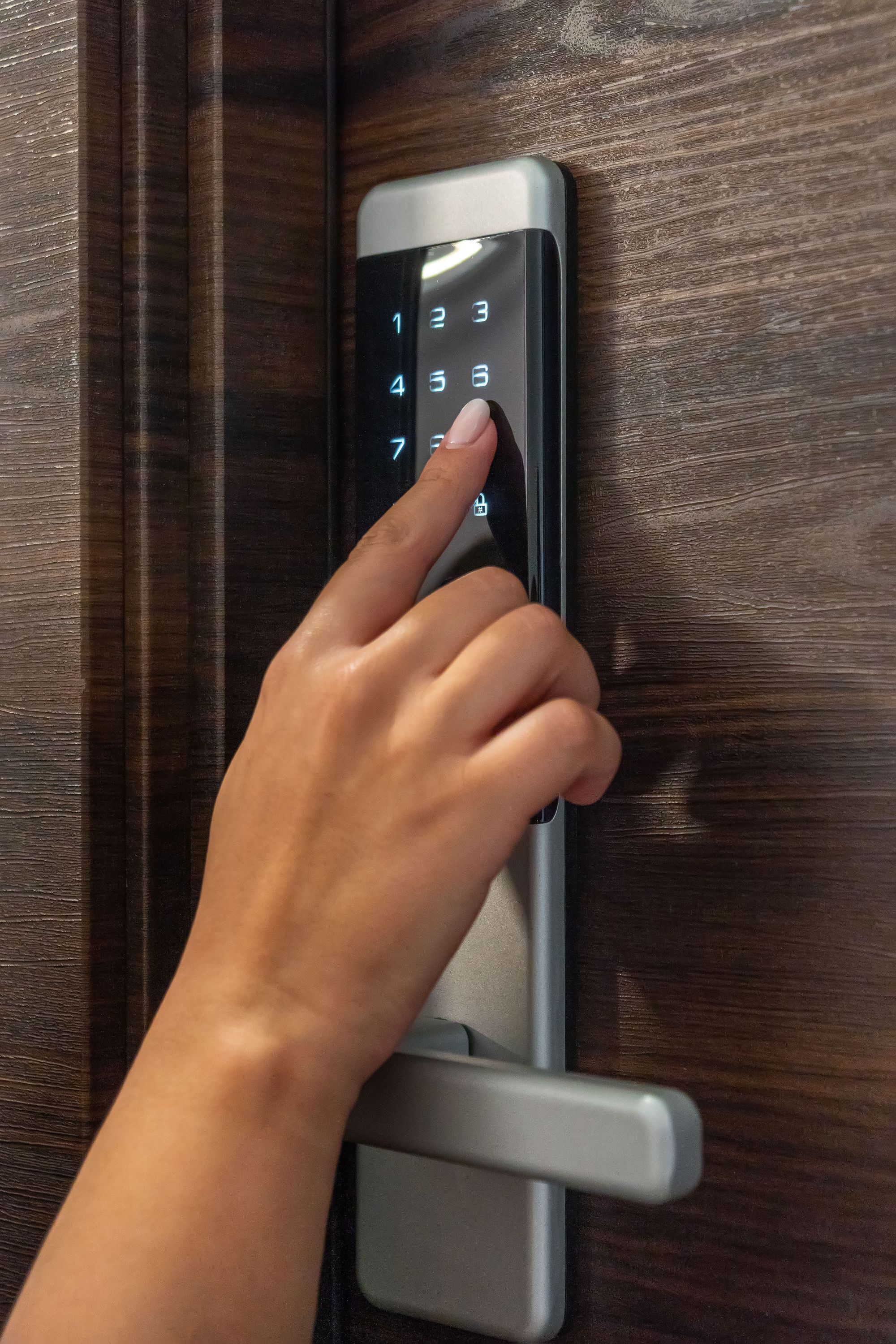 A hand using a numeric keypad on a modern door lock.