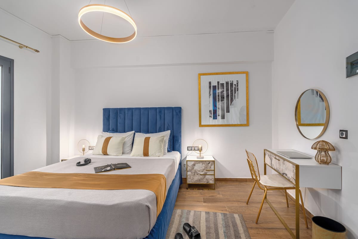 A modern bedroom with a bed, bedside table, desk, chair, and a large framed artwork.