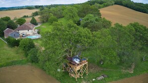 A wooden hot air balloon house with a hot air balloon, a swimming pool, and a house in the background. - Les Bulles Perchées de Lartigue (Margouet-Meymes)