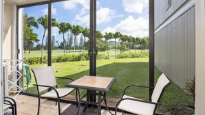 Une terrasse avec une table et des chaises, un tuyau d’arrosage et une vue sur une pelouse verdoyante et des arbres.