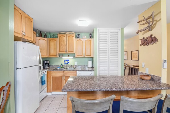 A kitchen with wooden cabinets, a granite countertop, and a white refrigerator. - Iconic Turtle Bay! Walk to beach -Full Kitchen - 2 Full Baths - Rated 9.6 of 10! (Kahuku)
