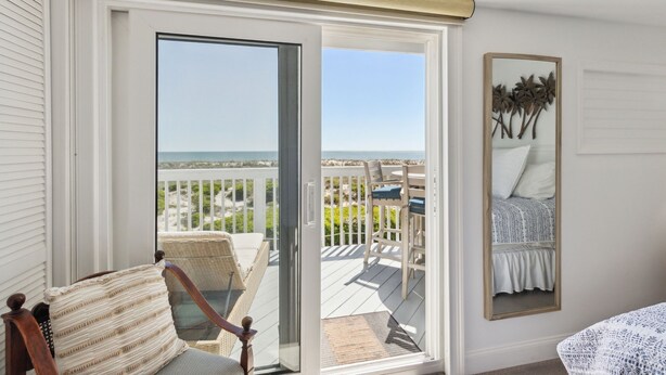 A room with a sliding glass door leading to a balcony with a view of the beach. There is a wicker chair and a small table on the balcony. - 95100 Sandpiper - Beautiful Oceanfront 2 BR Condo on Amelia Island (Fernandina Beach)