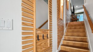 A wooden staircase with a modern design, a wall-mounted light switch, and a wooden panel with hooks. - 95100 Sandpiper - Beautiful Oceanfront 2 BR Condo on Amelia Island (Fernandina Beach)
