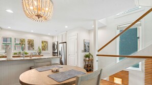 A modern kitchen with white cabinetry, a central island, and a dining area with a round table and chairs. - 95100 Sandpiper - Beautiful Oceanfront 2 BR Condo on Amelia Island (Fernandina Beach)