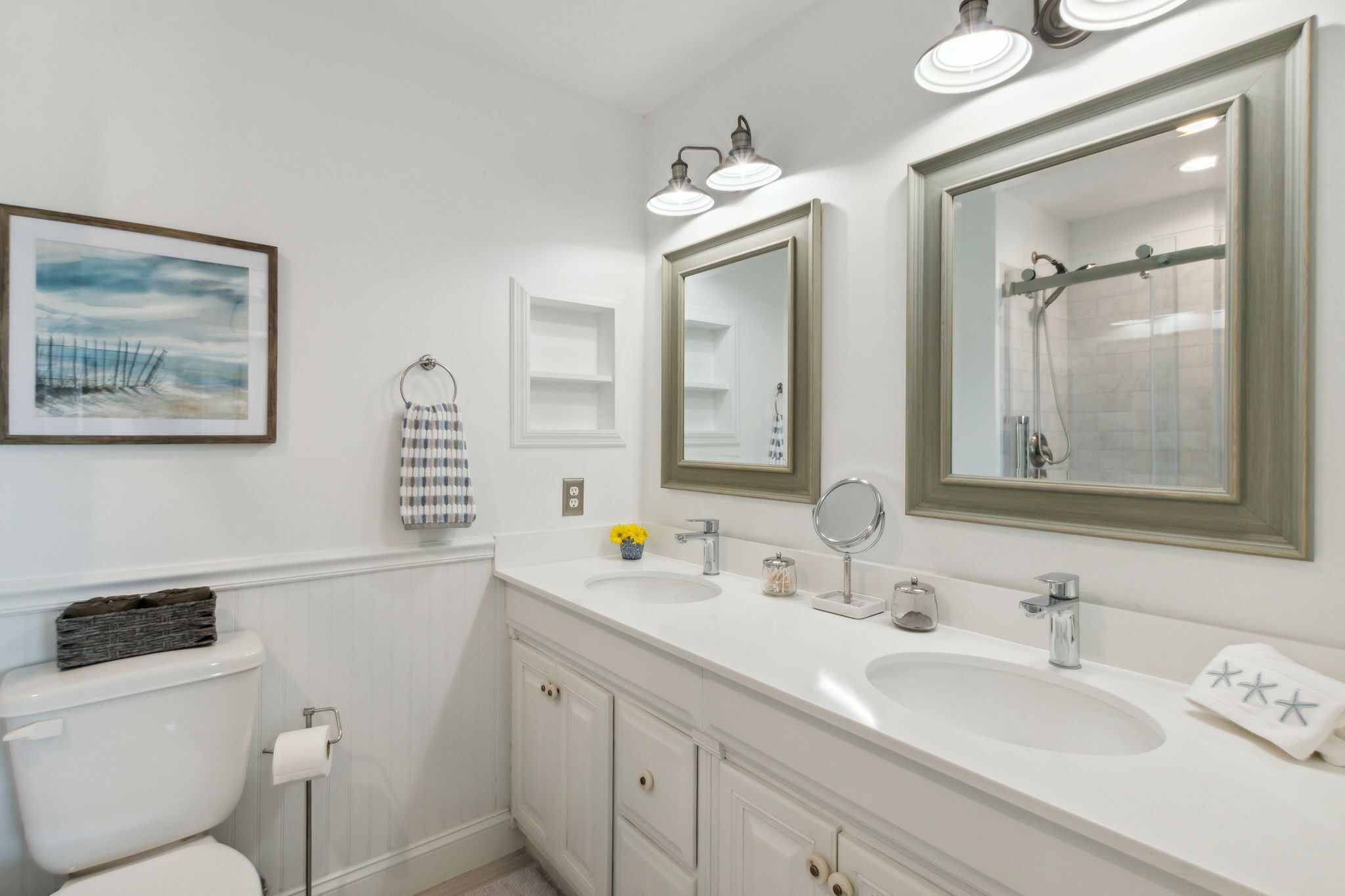 A bathroom with a toilet, two sinks, a mirror, and a shower.