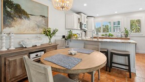 A modern kitchen with white cabinetry, a central island, and a dining area with a round table and bar stools. - 95100 Sandpiper - Beautiful Oceanfront 2 BR Condo on Amelia Island (Fernandina Beach)