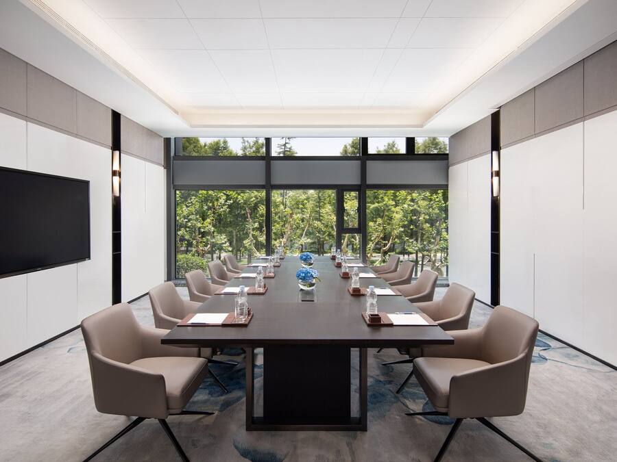 A conference room with a long table, beige chairs, and a large screen.