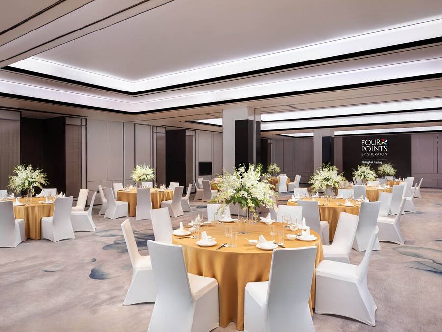 Un amplio salón de banquetes con mesas redondas dispuestas para comer, sillas blancas y centros de mesa florales.