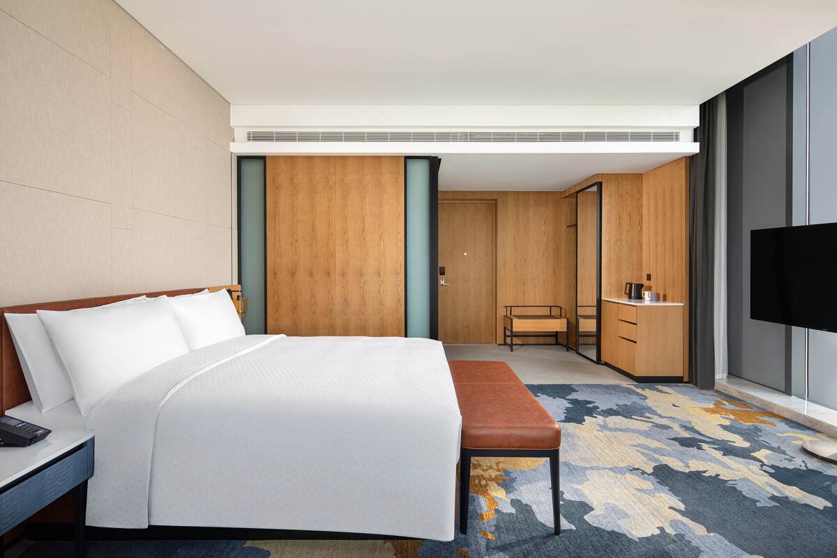 A hotel room with a bed, a desk, a chair, a TV, and a wardrobe.