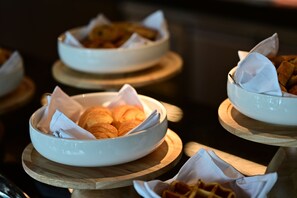 Un bufé con varias fuentes de comida, incluyendo pasteles y pan, dispuestas sobre pedestales de madera.