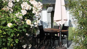 A patio with a table and chairs, surrounded by lush greenery and white flowers. - LE COLVERT 4-star furnished holiday home with PRIVATE JACUZZI and PRIVATE SAUNA (Le Hanouard)