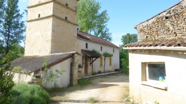 Un edificio de piedra tradicional con una torre, una estructura pequeña adosada y un camino de grava que conduce a la entrada.