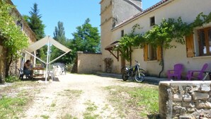 Un patio con un muro de piedra, una zona de estar cubierta y un edificio con una torre.