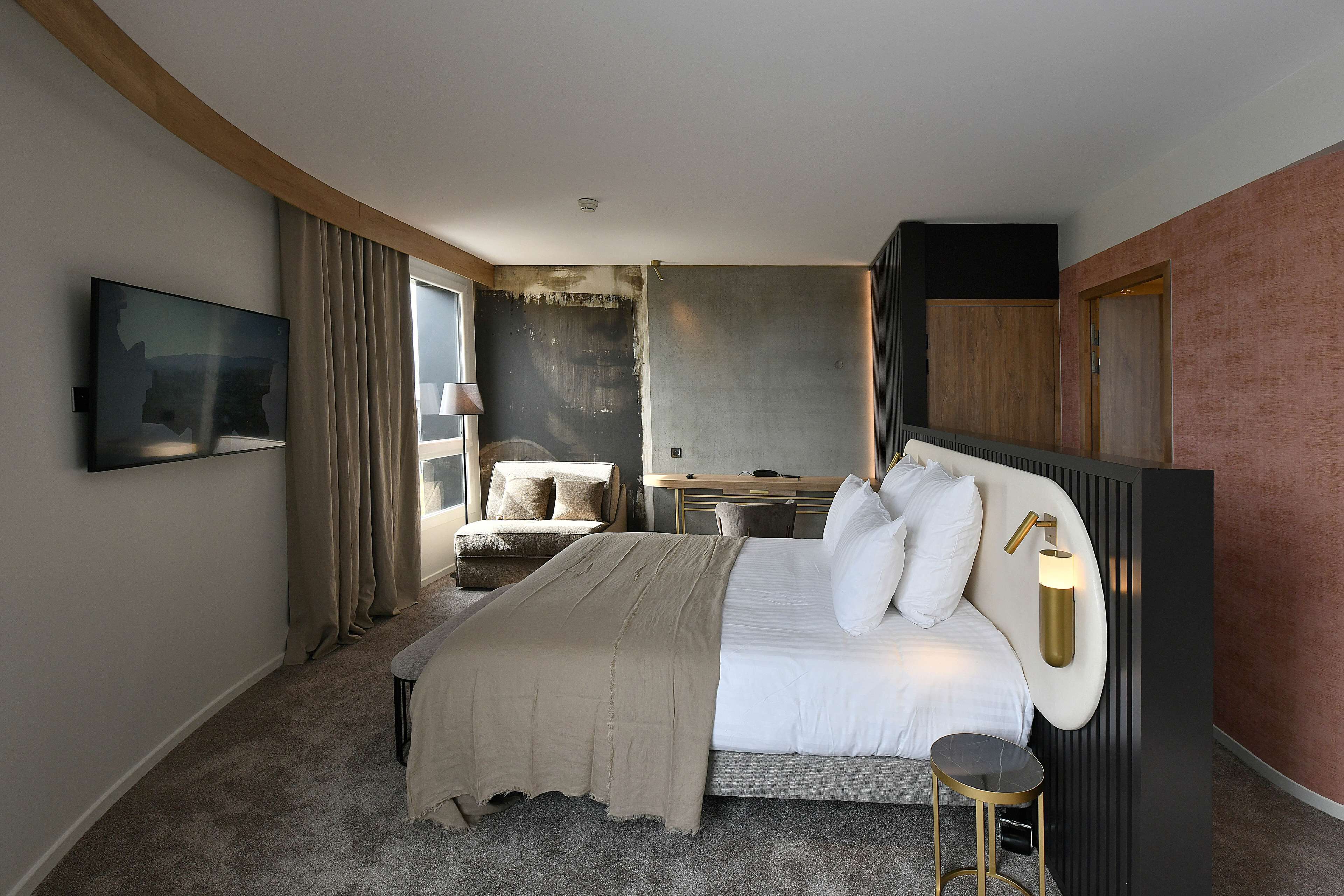 A modern hotel room with a large bed, a desk, and a TV mounted on the wall.