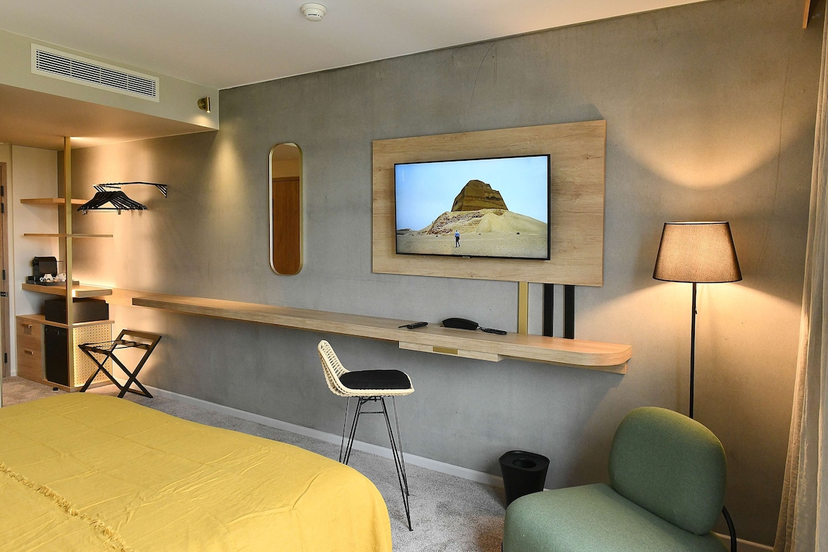 Une chambre d’hôtel équipée d’un lit, d’un bureau, d’une chaise, d’un téléviseur fixé au mur et d’une lampe.
