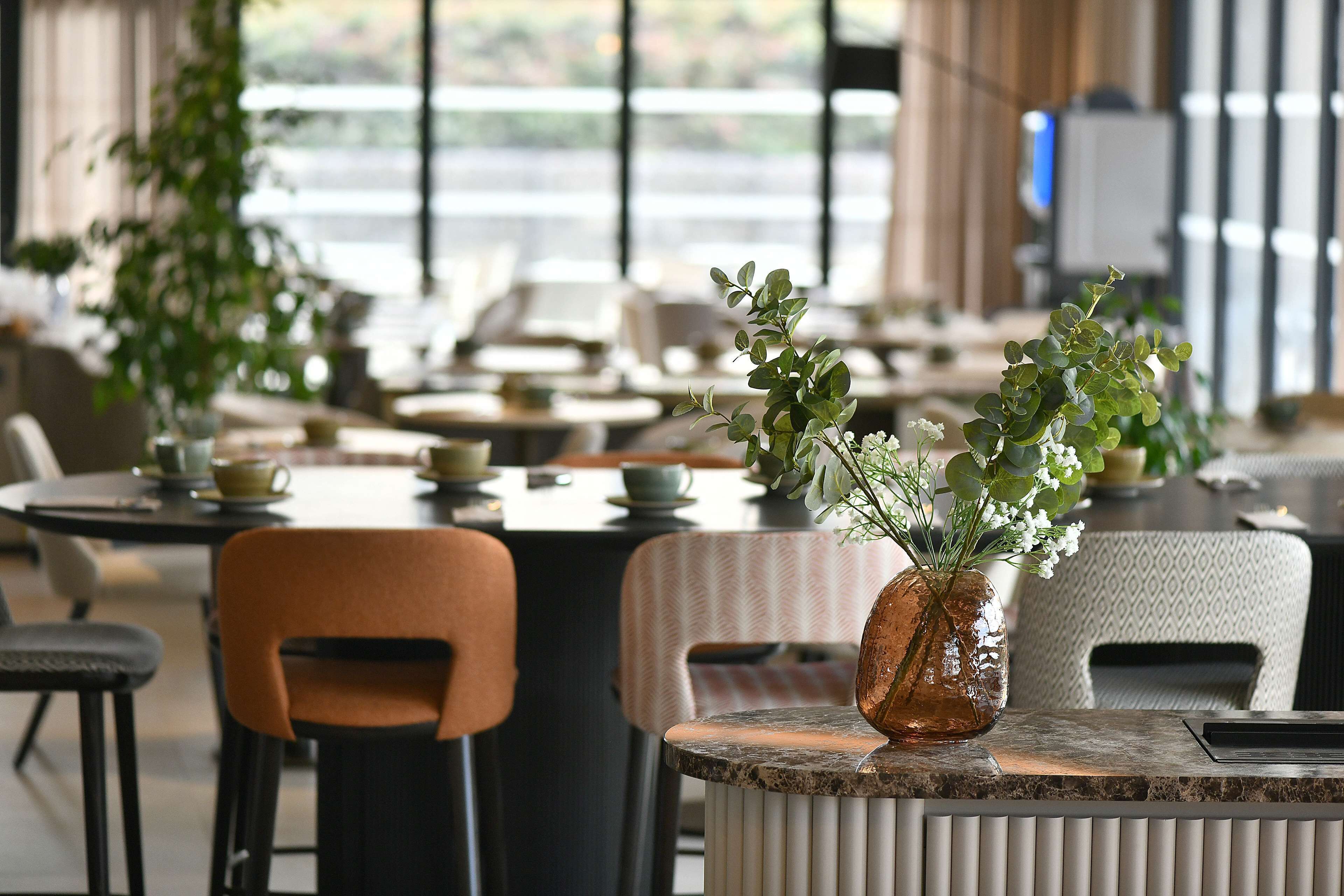 A restaurant with tables and chairs, some with plants.