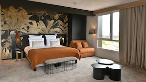 A modern bedroom with a large bed, a sofa, a small table, and a window with curtains. - Golden Tulip Reims (Bezannes)