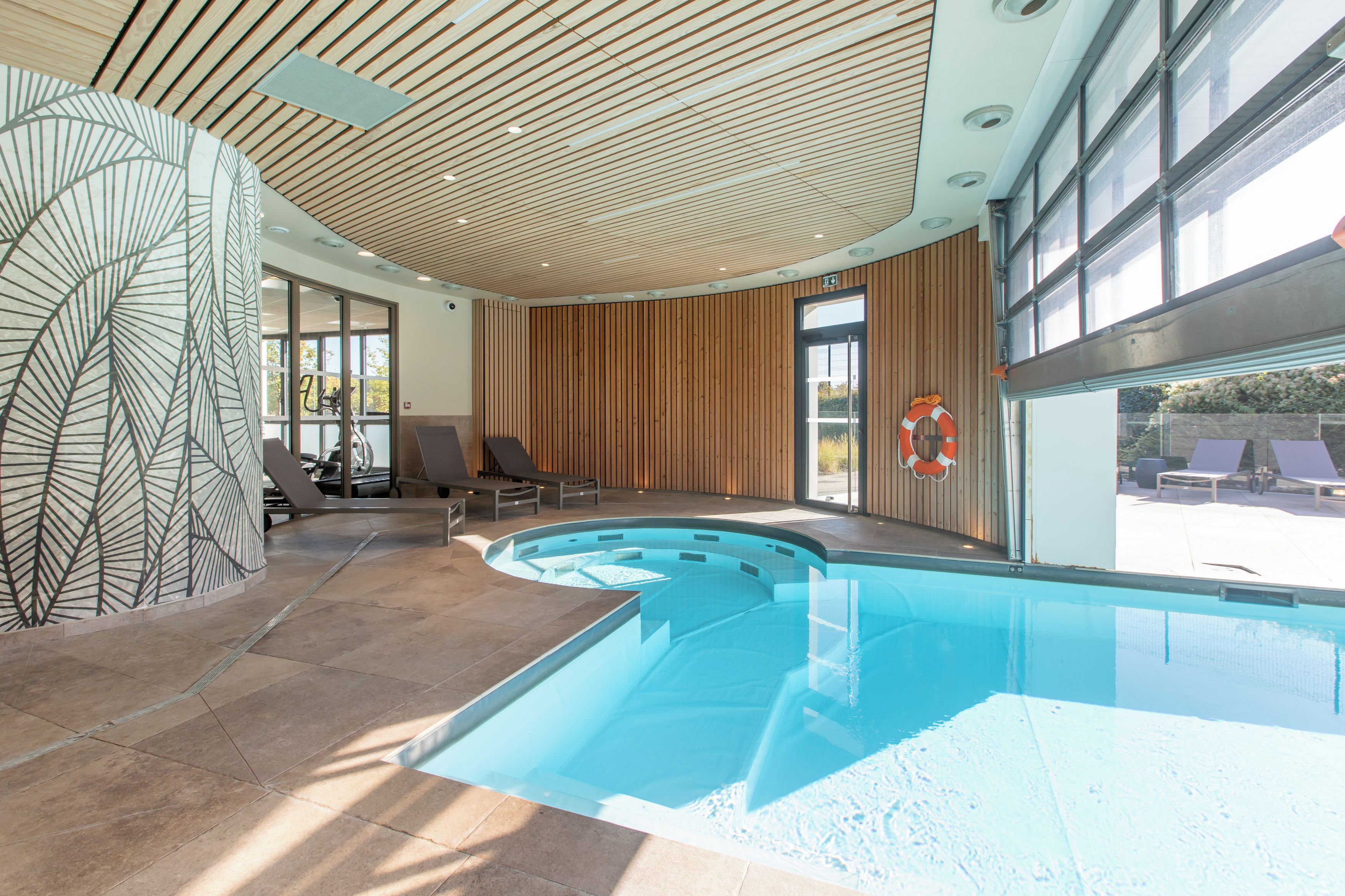 An indoor swimming pool with a wooden ceiling, lounge chairs, and a lifebuoy.