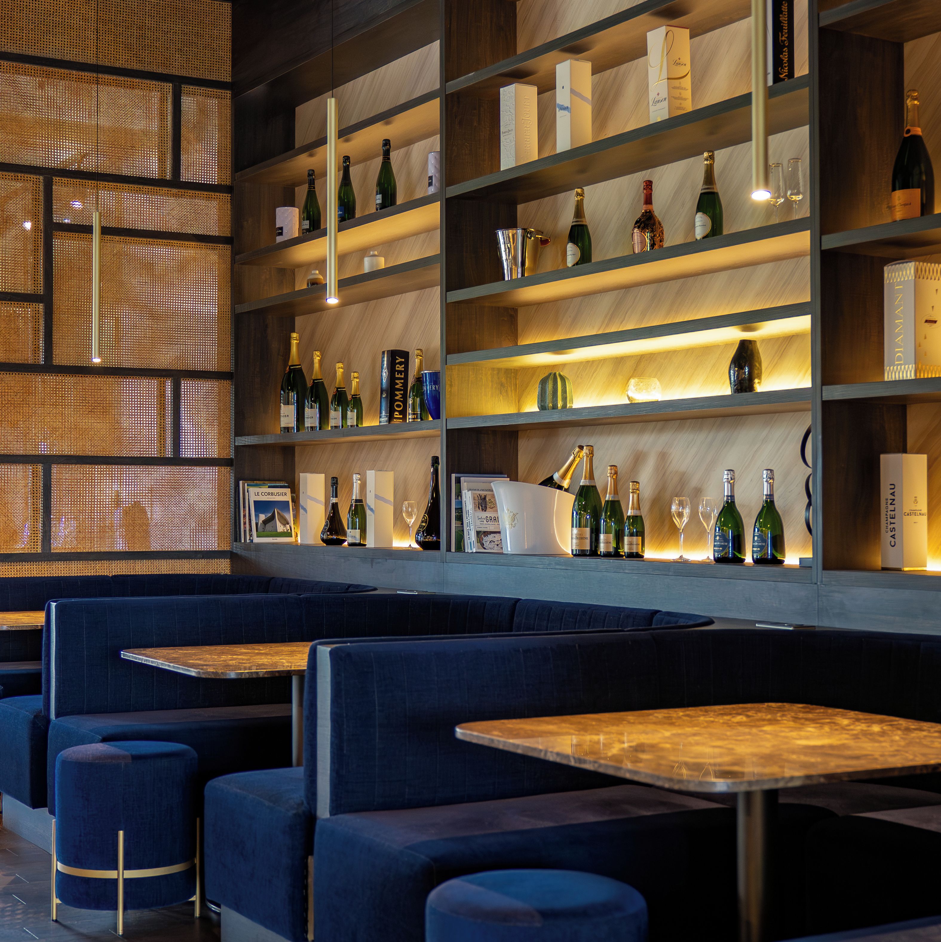 Zona de bar con varias estanterías llenas de botellas y copas, asientos con mesas y una pared decorativa con diseño perforado.