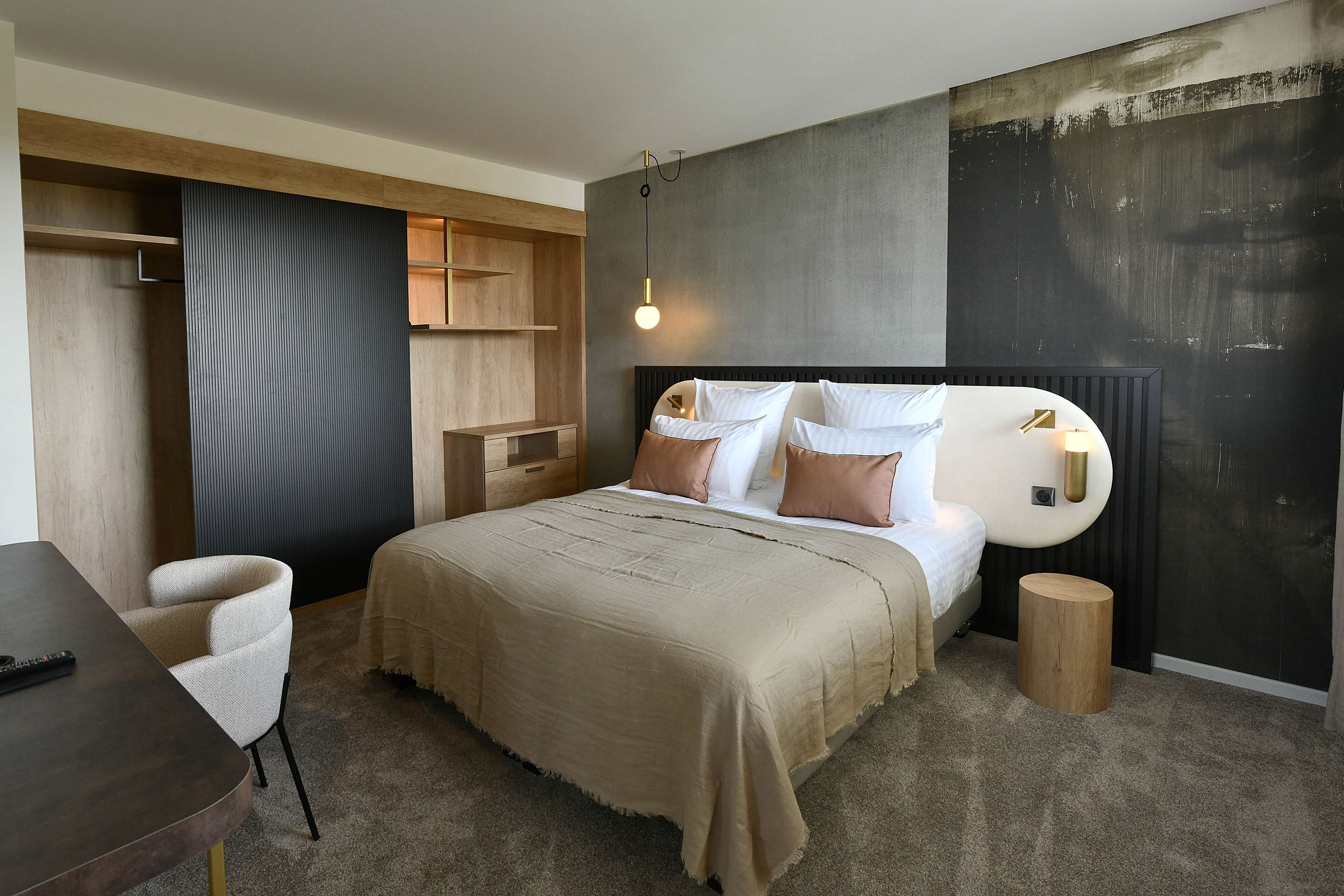 A modern bedroom with a large bed, bedside tables, a chair, and a small wooden stool.