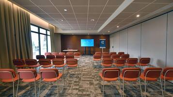 Un salón de conferencias con filas de sillas anaranjadas, una pantalla grande y un atril.