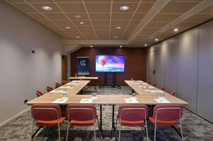 Ett konferensrum med ett långt bord, röda stolar, en projektorduk och ett golv täckt av matta.