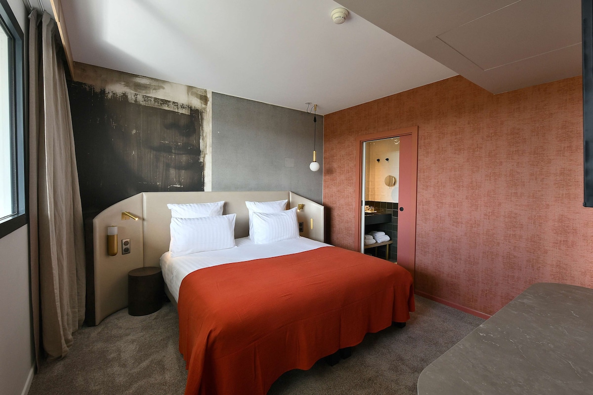 Une chambre d’hôtel avec un lit, une table de chevet, un miroir et une porte.