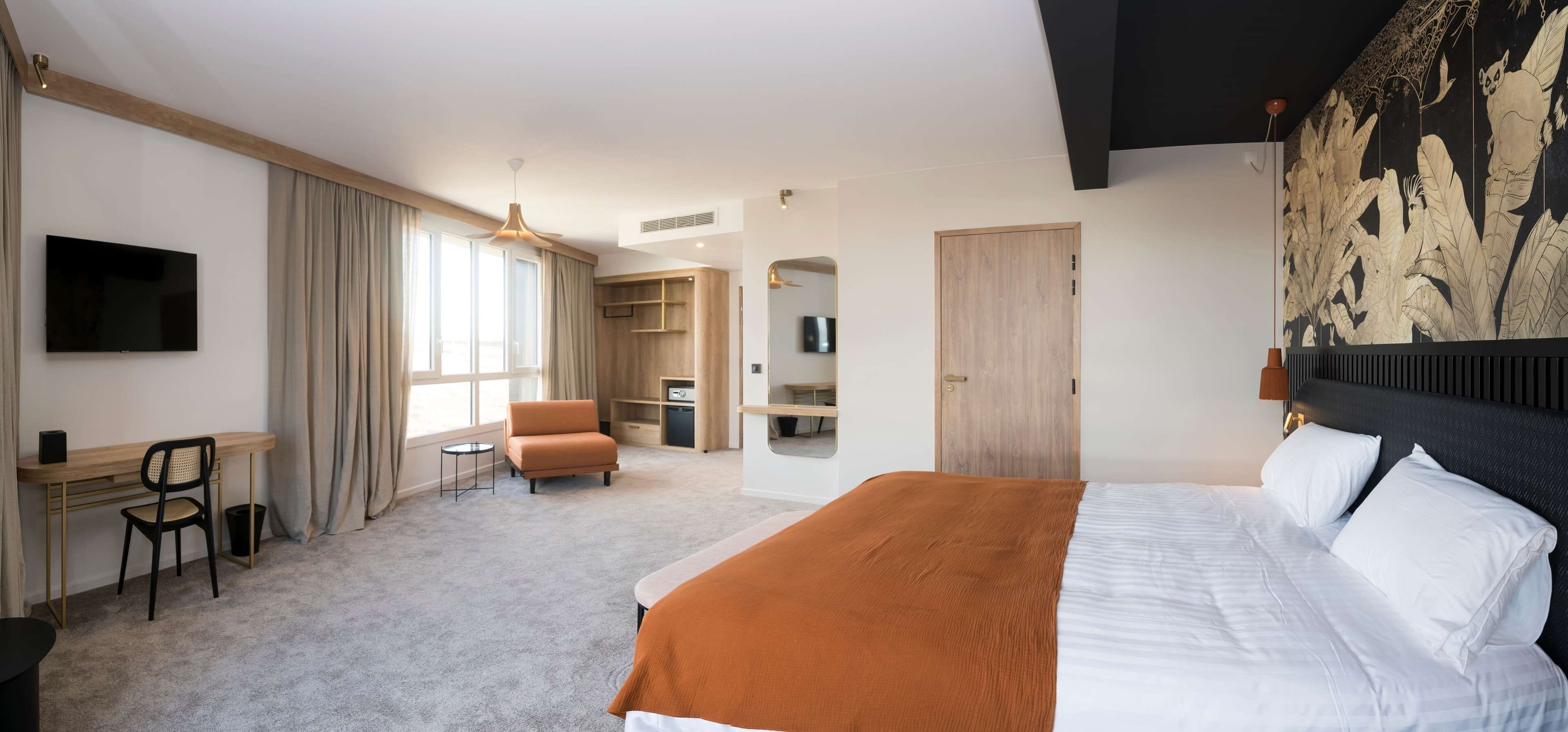 A hotel room with a large bed, a desk with a chair, a sofa, and a television.