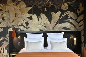 Une chambre à coucher avec un grand lit, deux tables de chevet et un mur orné d’un motif de feuilles.