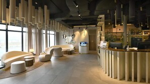 A modern hotel lobby with a reception desk, seating area, and large windows. - Golden Tulip Reims (Bezannes)