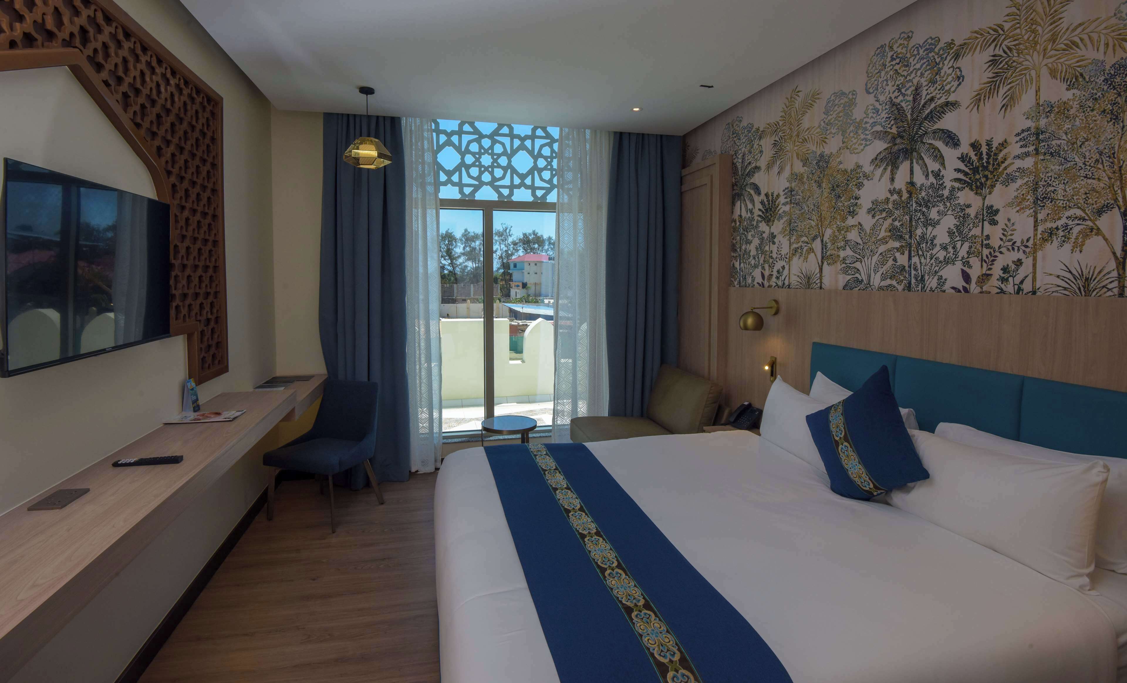 A hotel room with a large bed, a desk, a chair, and a TV.